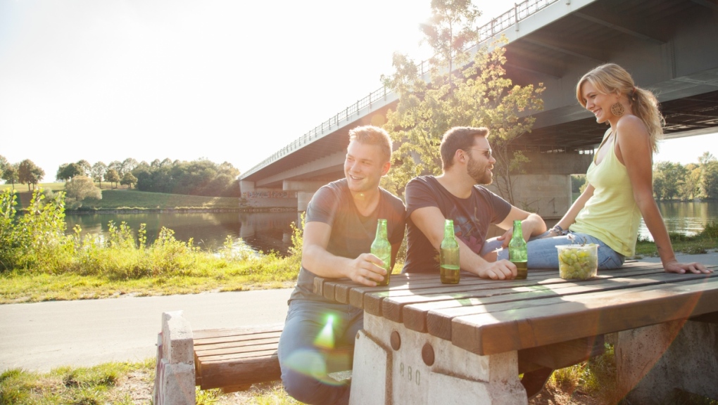 Three friends sit together at a park picnic table near a river. (Getty Images) 