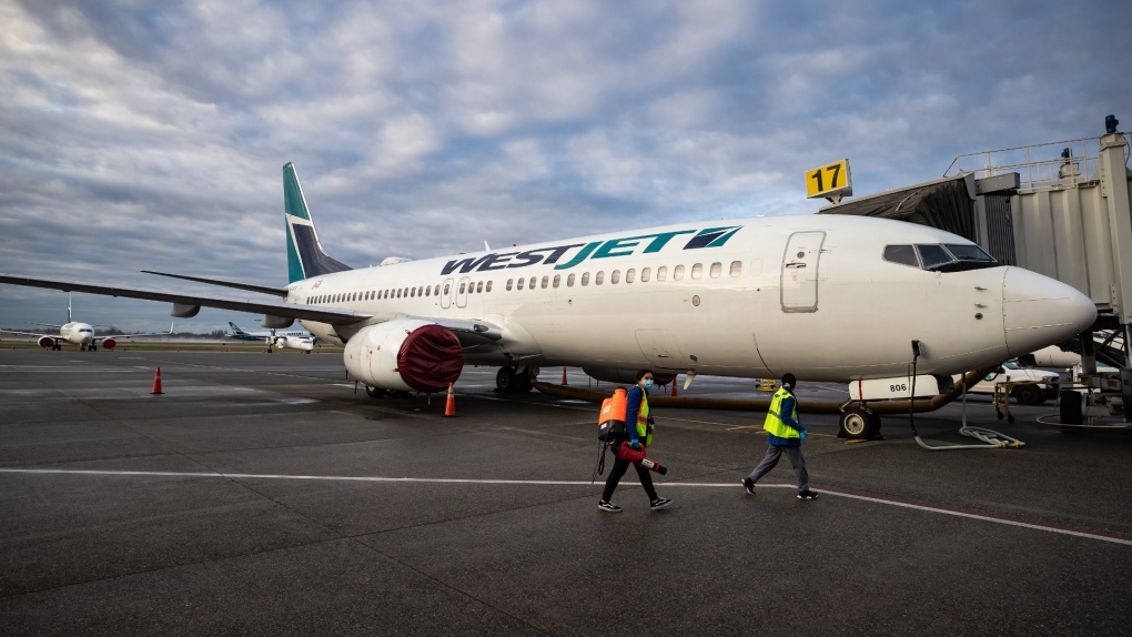 A worker carrying a disinfectant sprayer walks past a WestJet Airlines Boeing 737-800 aircraft, after cleaning another plane at Vancouver International Airport, in Richmond, B.C., on Jan. 21, 2021. (THE CANADIAN PRESS/Darryl Dyck) 