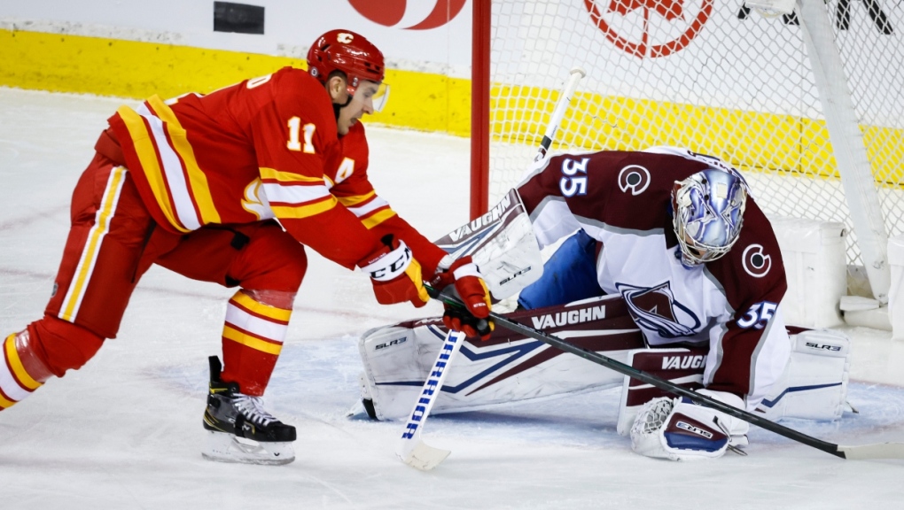 Colorado Avalanche goalie Darcy Kuemper, right, covers the puck as Calgary Flames' Mikael Backlund reaches for it during second period NHL hockey action in Calgary, Tuesday, March 29, 2022. (THE CANADIAN PRESS/Jeff McIntosh)