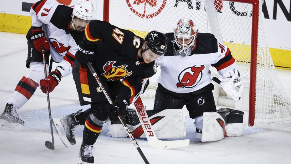 New Jersey Devils goalie Vitek Vanecek, right, guards the net as Calgary Flames forward Connor Zary, centre, chases a loose puck while defenceman Jonas Siegenthaler looks on during second period NHL hockey action in Calgary, Alta., Saturday, Dec. 9, 2023. THE CANADIAN PRESS/Jeff McIntosh