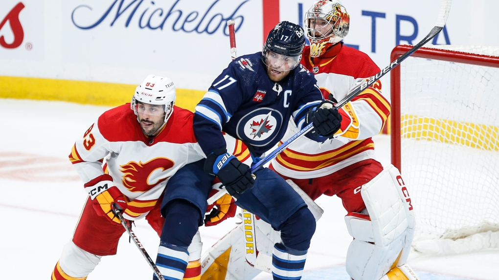 Calgary Flames' Jonathan Aspirot (83) defends against Winnipeg Jets' Adam Lowry (17) in front of goaltender Dustin Wolf (32) during second period NHL pre-season game action in Winnipeg, Wednesday, Sept. 27, 2023. THE CANADIAN PRESS/John Woods
